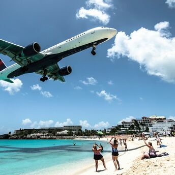 Airplane flying low over a crowded beach, with onlookers watching and taking photos