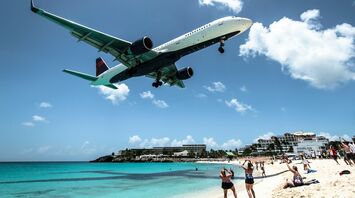 Airplane flying low over a crowded beach, with onlookers watching and taking photos