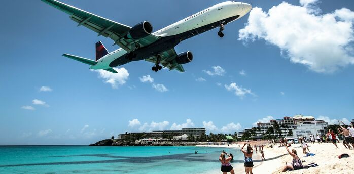 Airplane flying low over a crowded beach, with onlookers watching and taking photos