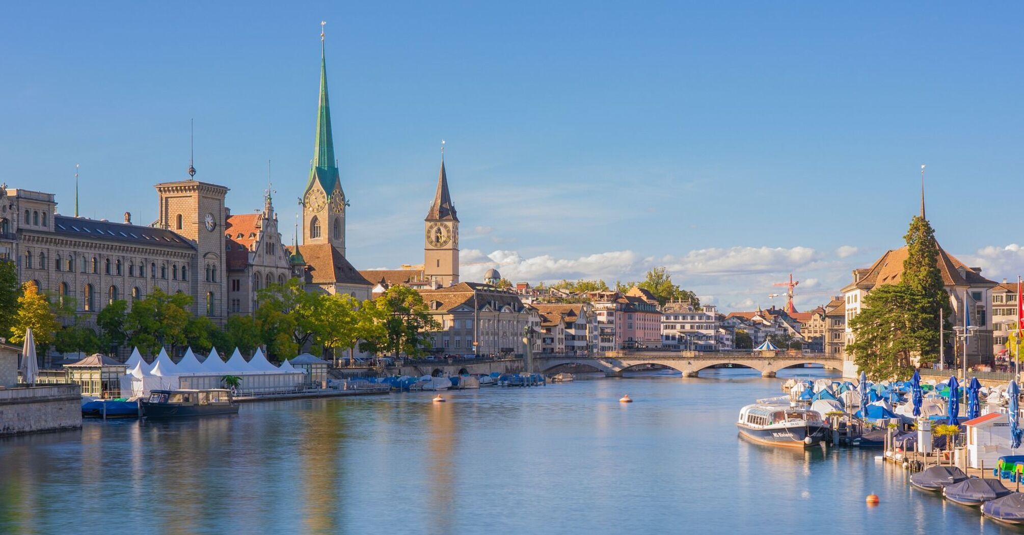 A scenic view of Zurich's historic buildings along the river, with clear blue skies and vibrant greenery