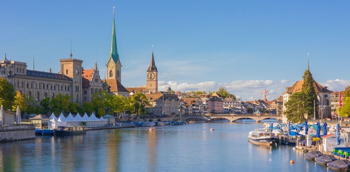 A scenic view of Zurich's historic buildings along the river, with clear blue skies and vibrant greenery