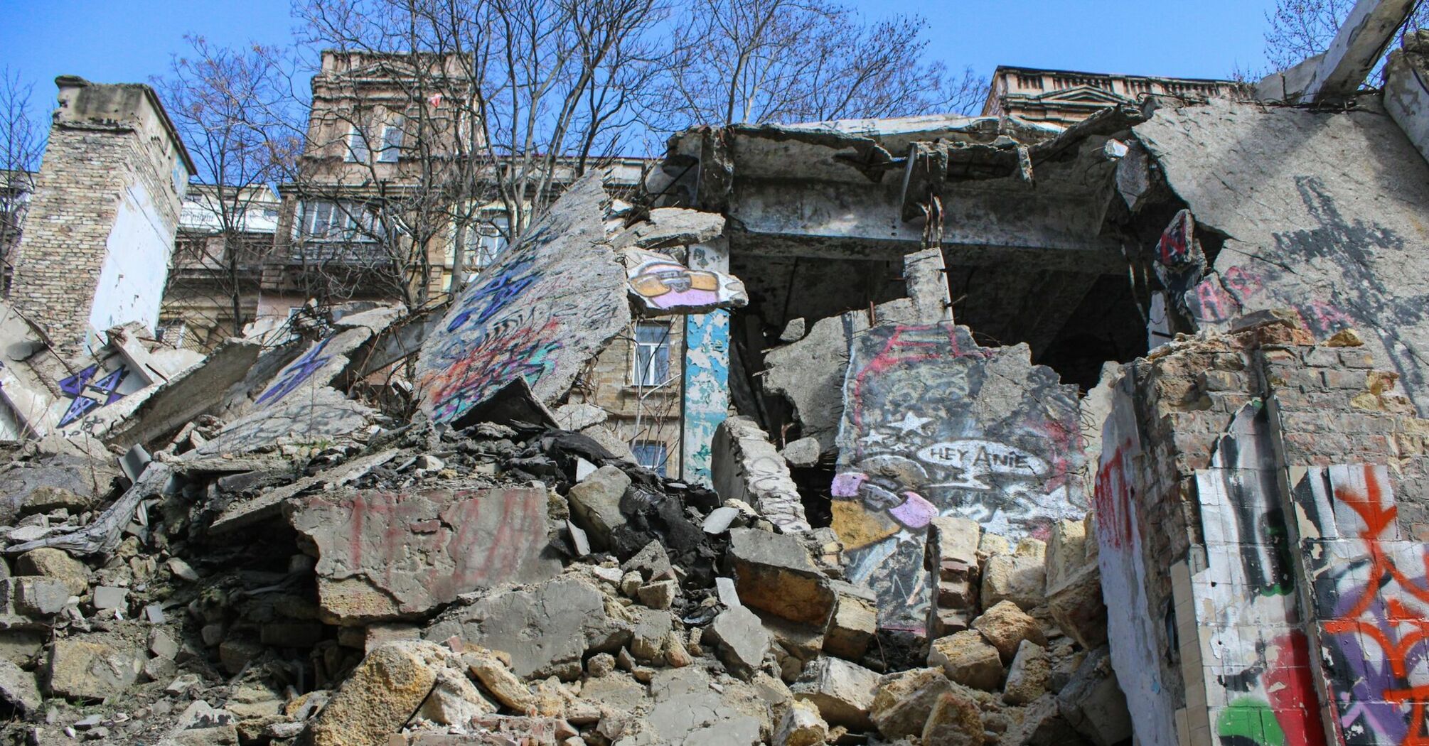 A severely damaged building with collapsed concrete and graffiti