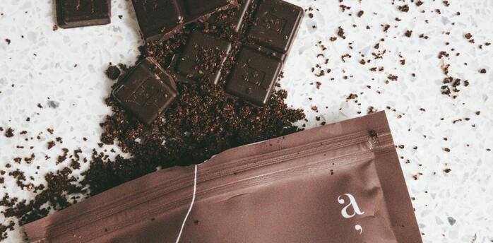 A close-up of dark chocolate squares on a light surface with crumbled pieces surrounding them