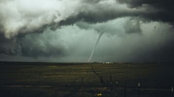 Dark tornado funnel on the horizon with stormy skies