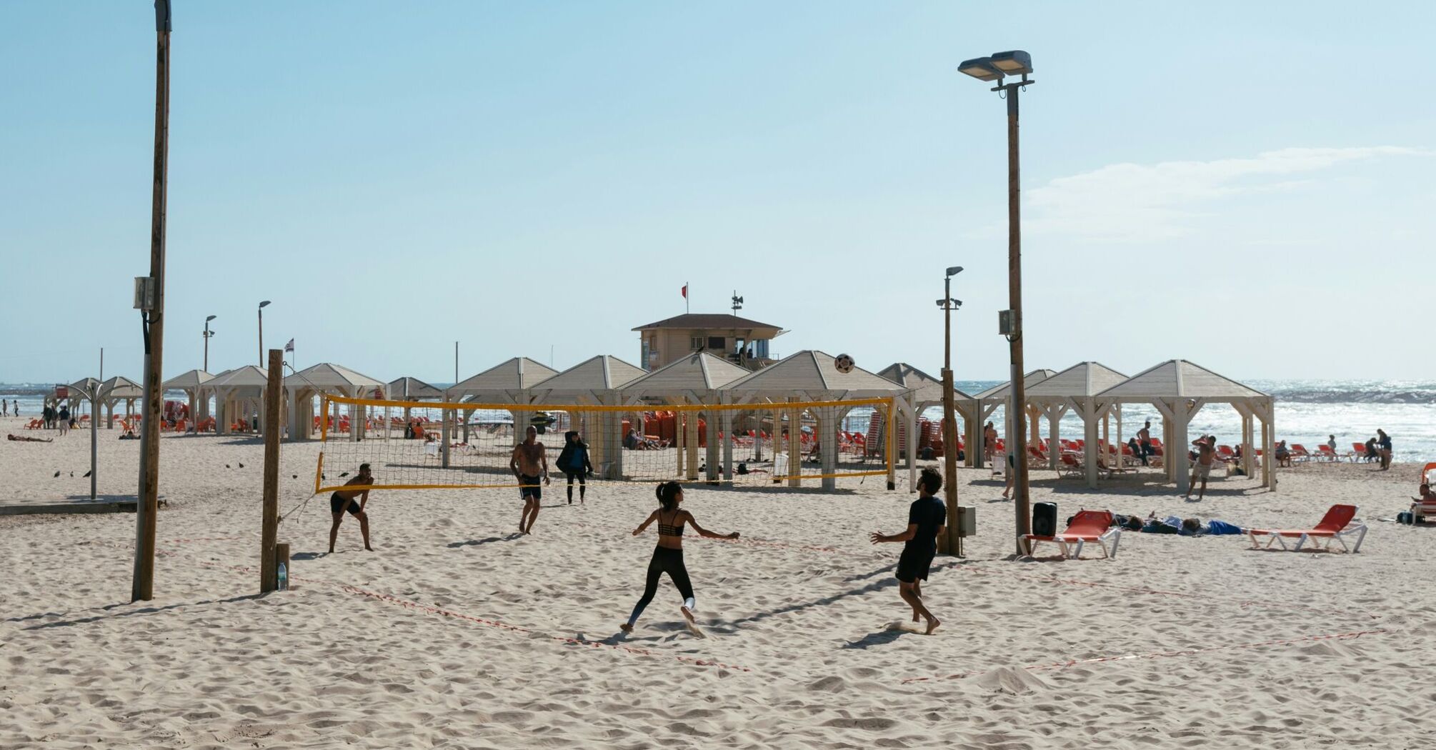A sunny beach scene with people playing volleyball
