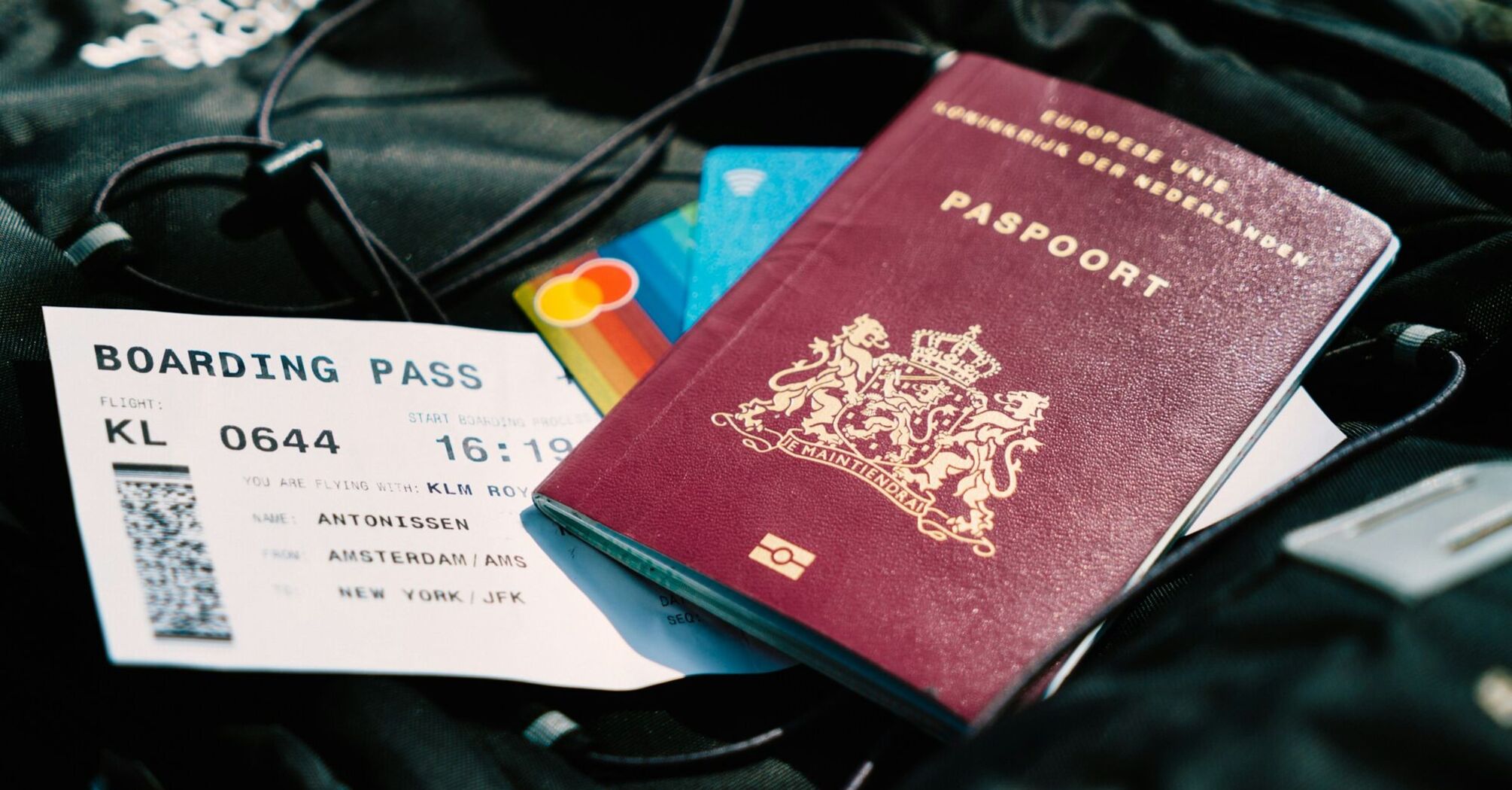 Travel essentials including a passport, boarding pass, and a black backpack with credit cards on top, ready for an international flight