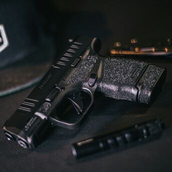 A handgun and magazine lying on a dark surface with a cap in the background