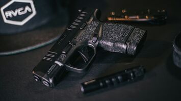 A handgun and magazine lying on a dark surface with a cap in the background