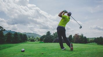Golfer in bright yellow shirt swinging a club on a sunny golf course with hills in the background