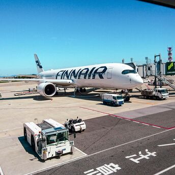 A Finnair airplane docked at an airport terminal with ground service equipment and personnel visible