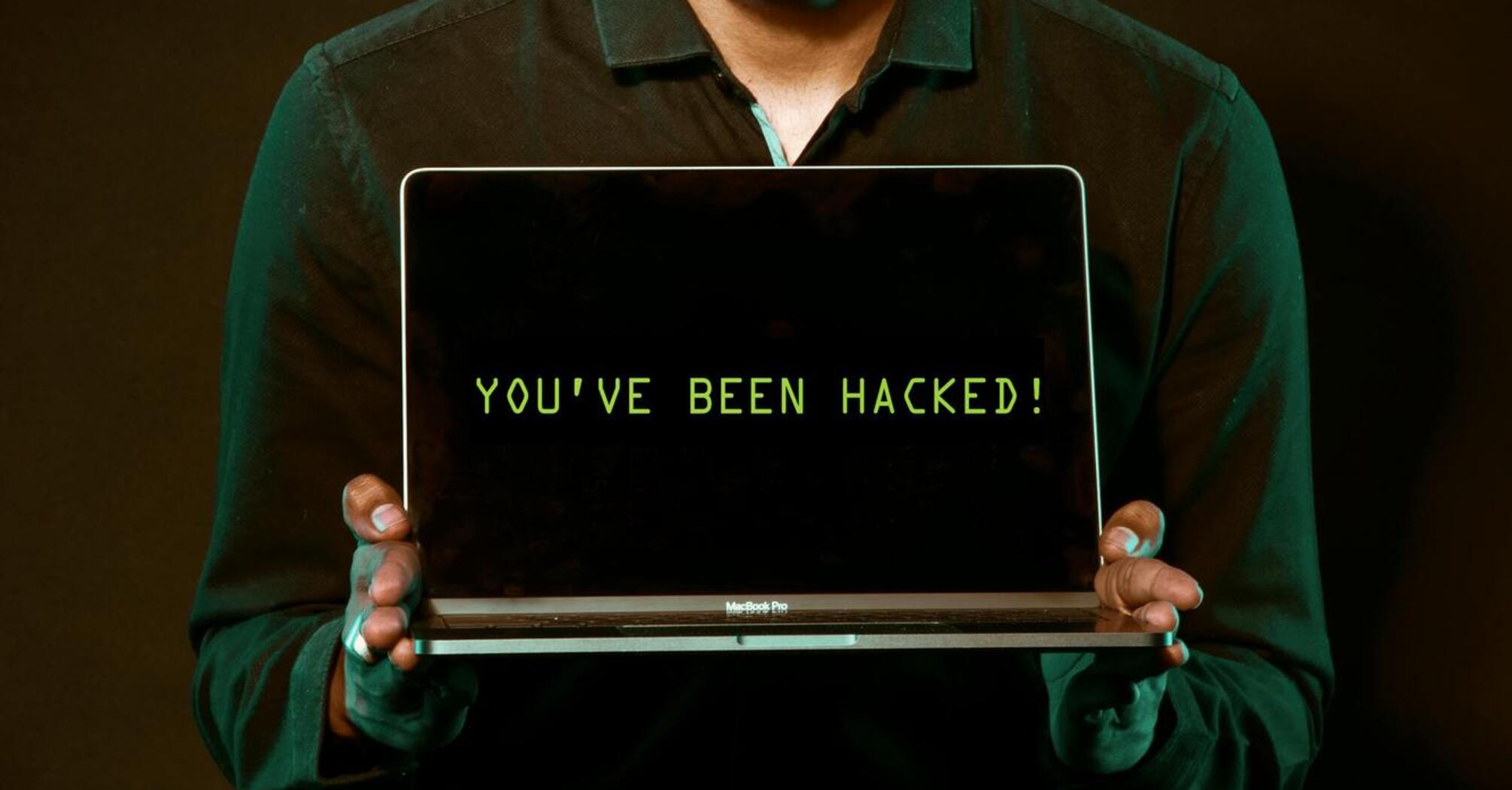 Man holding a laptop displaying 'YOU'VE BEEN HACKED!' message