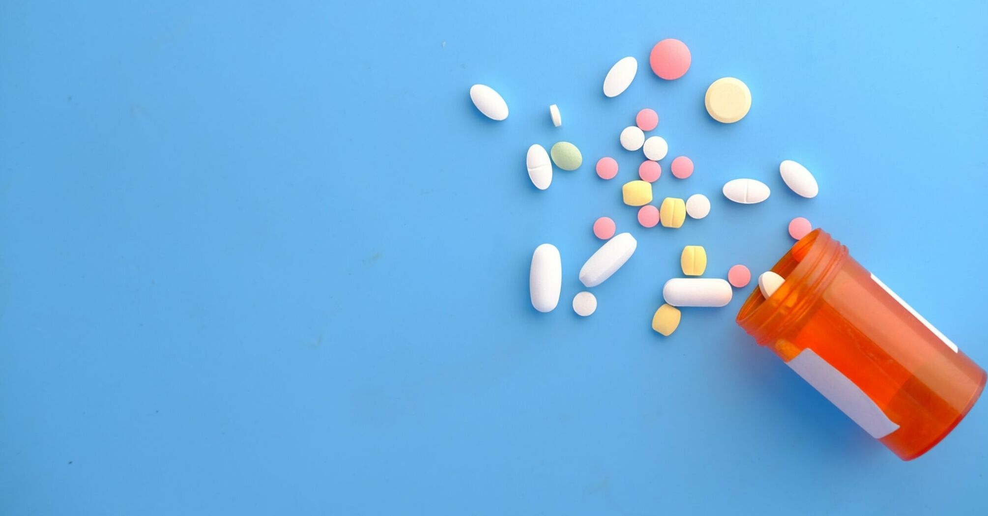 Assorted pills spilled from an orange  bottle onto a blue background