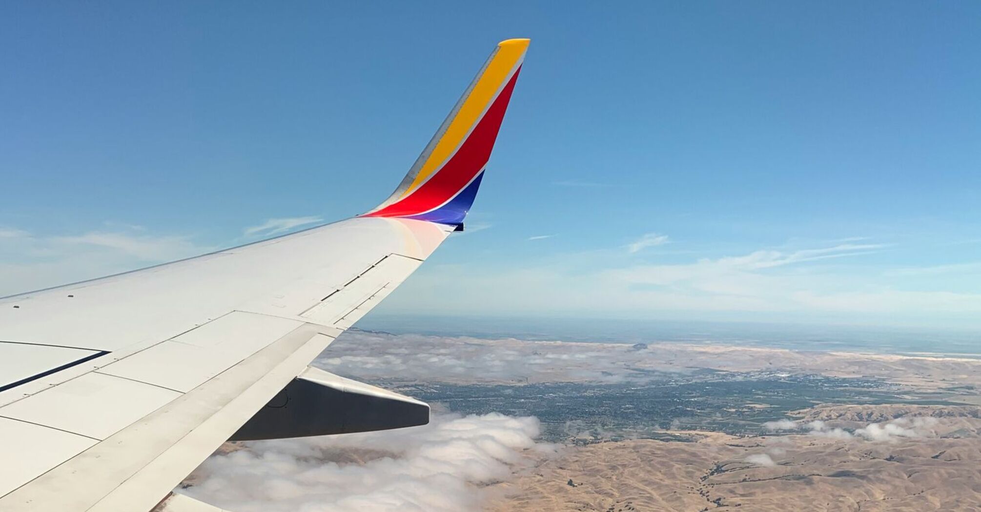 View from a Southwest Airlines plane window showing the wing and landscape below with clouds and hills