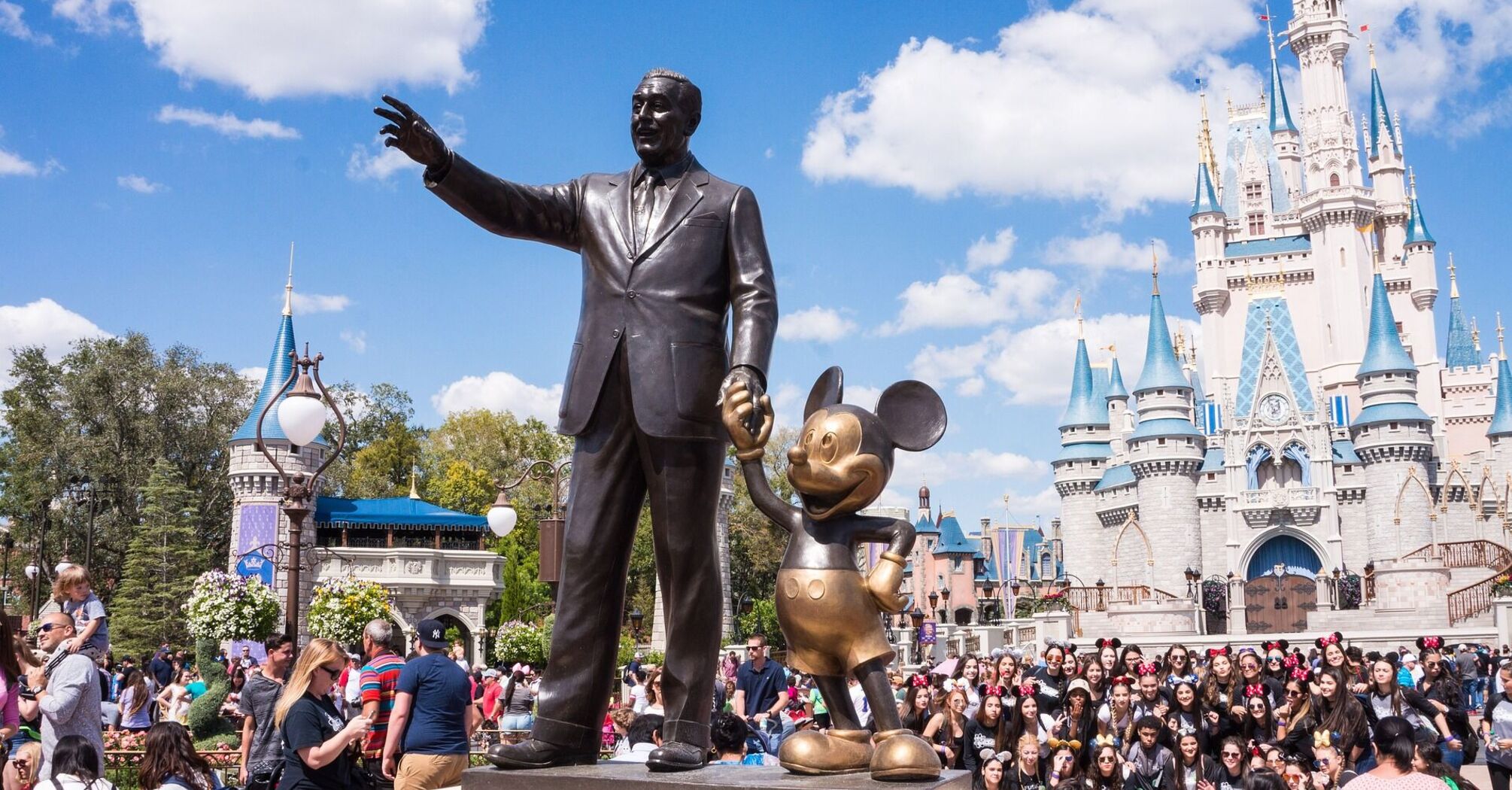 Statue of Walt Disney holding hands with Mickey Mouse in front of Cinderella Castle at a crowded Disney theme park