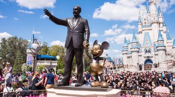 Statue of Walt Disney holding hands with Mickey Mouse in front of Cinderella Castle at a crowded Disney theme park