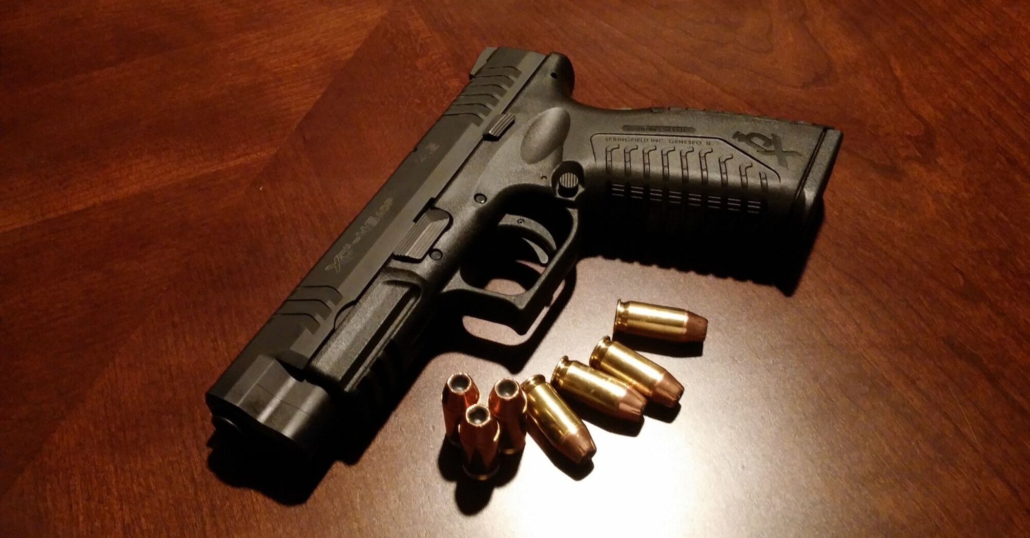 Handgun with a magazine beside it and several bullets scattered on a wooden surface