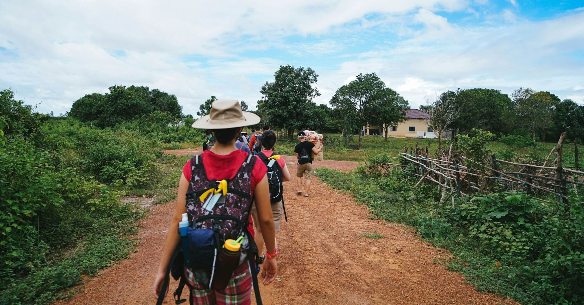 Tourists with backpacks walking on a rural path surrounded by greenery
