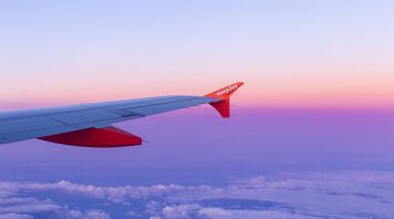 Wing of an easyJet airplane against a purple and pink sky at sunset, flying above the clouds