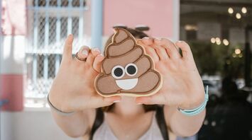 Person holding a cookie shaped like the poop emoji