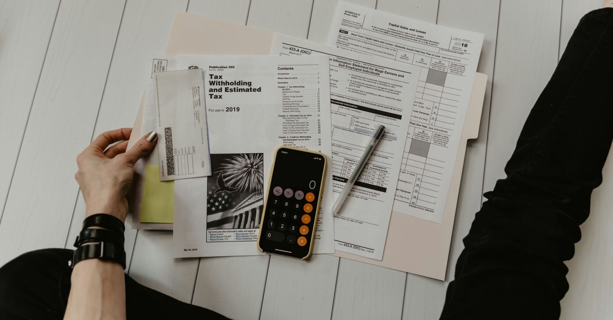 Person organizing various tax forms and documents with a calculator on a white wooden table