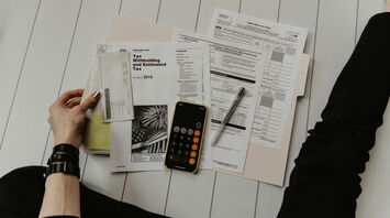 Person organizing various tax forms and documents with a calculator on a white wooden table