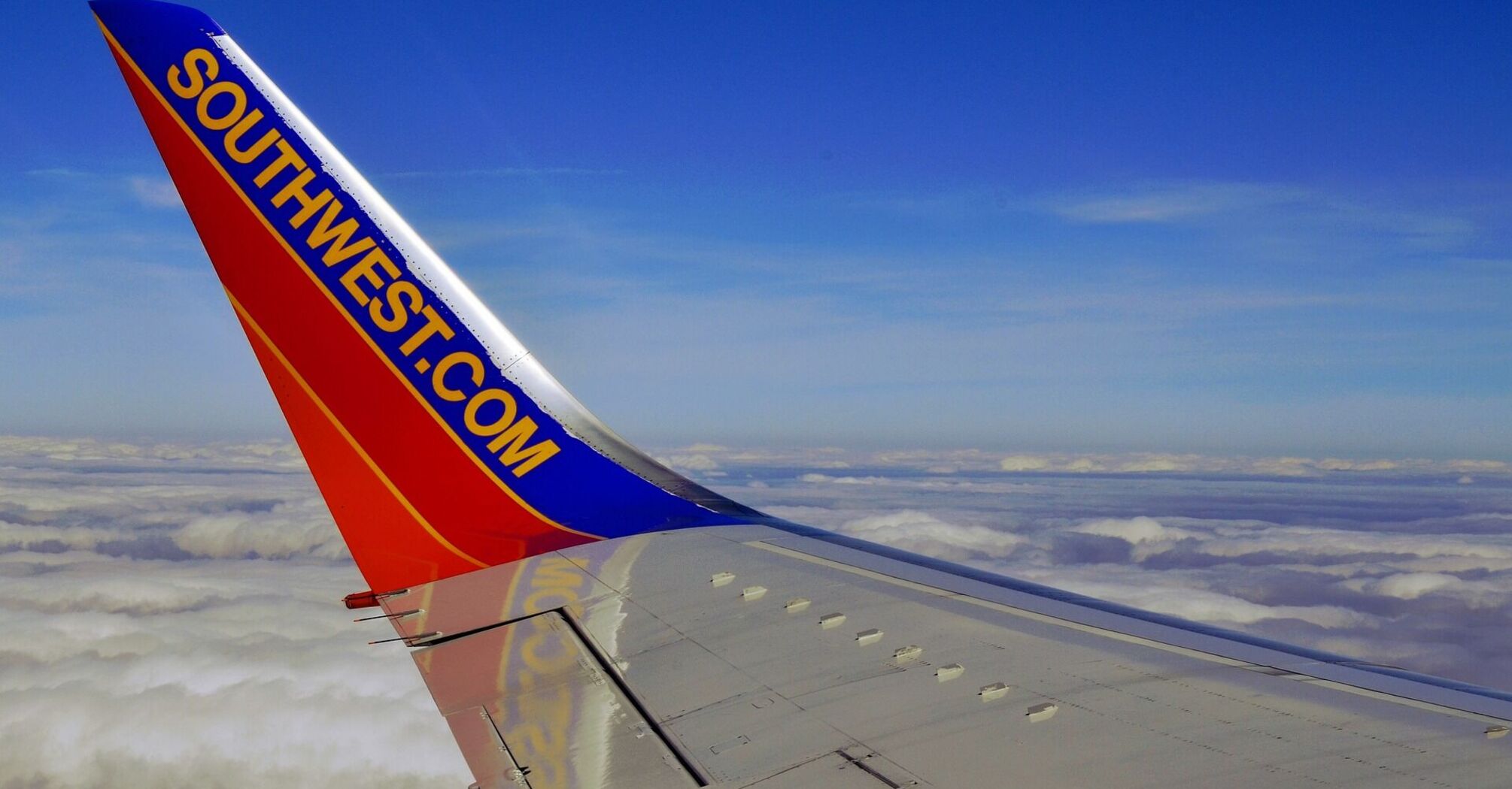 View from a Southwest Airlines airplane window showing wing with logo over clouds