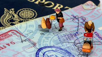 Miniature figures on a passport with travel stamps and visas, depicting travelers with luggage
