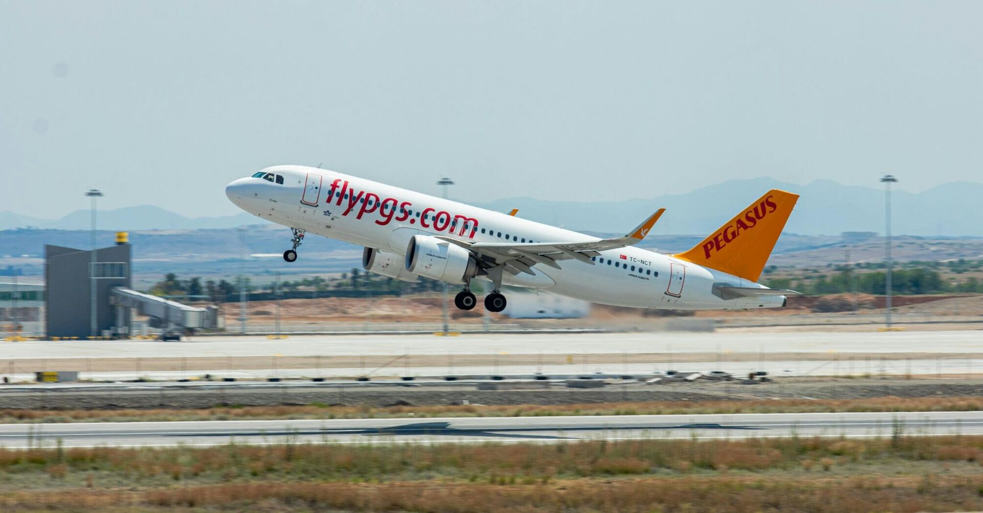 Pegasus Airlines aircraft taking off on a sunny day, showcasing the vibrant branding and colors of the airline