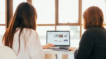 Two women talking while looking at laptop computer