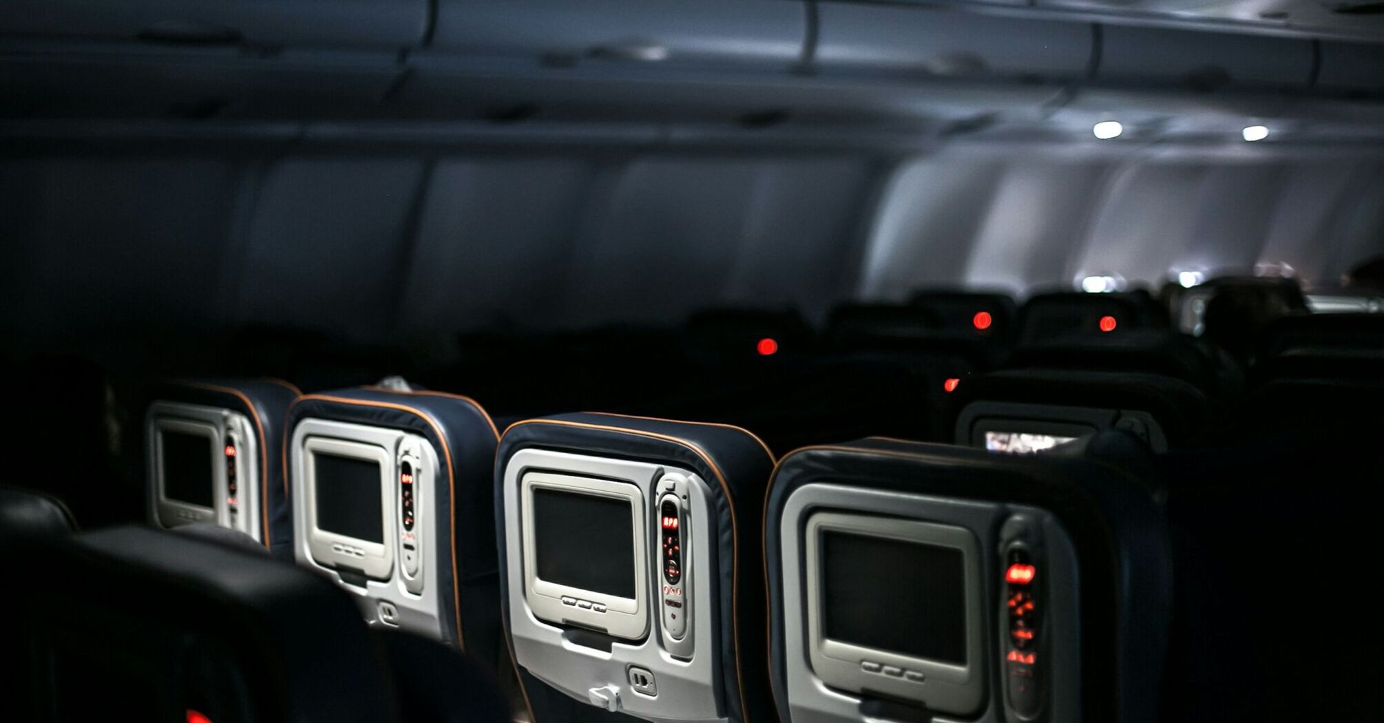 Interior view of an airplane cabin showing rows of seatback entertainment screens in dim lighting