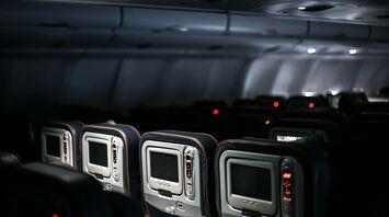 Interior view of an airplane cabin showing rows of seatback entertainment screens in dim lighting