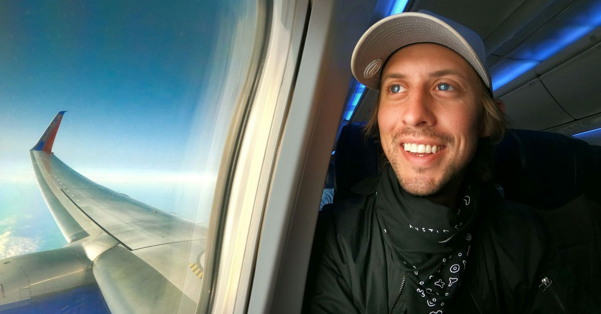 Smiling man enjoying a flight with a view of airplane wing through window