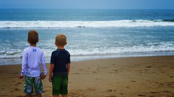 Two children are standing by the sea