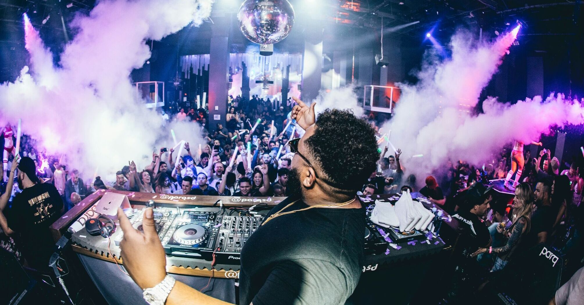 DJ playing at a nightclub with vibrant crowd and smoke effects