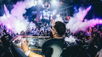 DJ playing at a nightclub with vibrant crowd and smoke effects