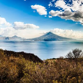 Grass field near body of water with Guatemala volcano at the background