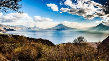 Grass field near body of water with Guatemala volcano at the background