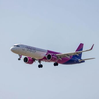 A large Wizz Air jetliner flying through a blue sky