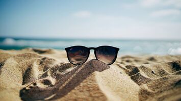 A pair of sunglasses lying on a sandy beach with a blurred ocean background