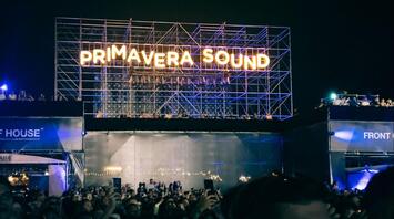 A large crowd of people in front of a stage with a sign