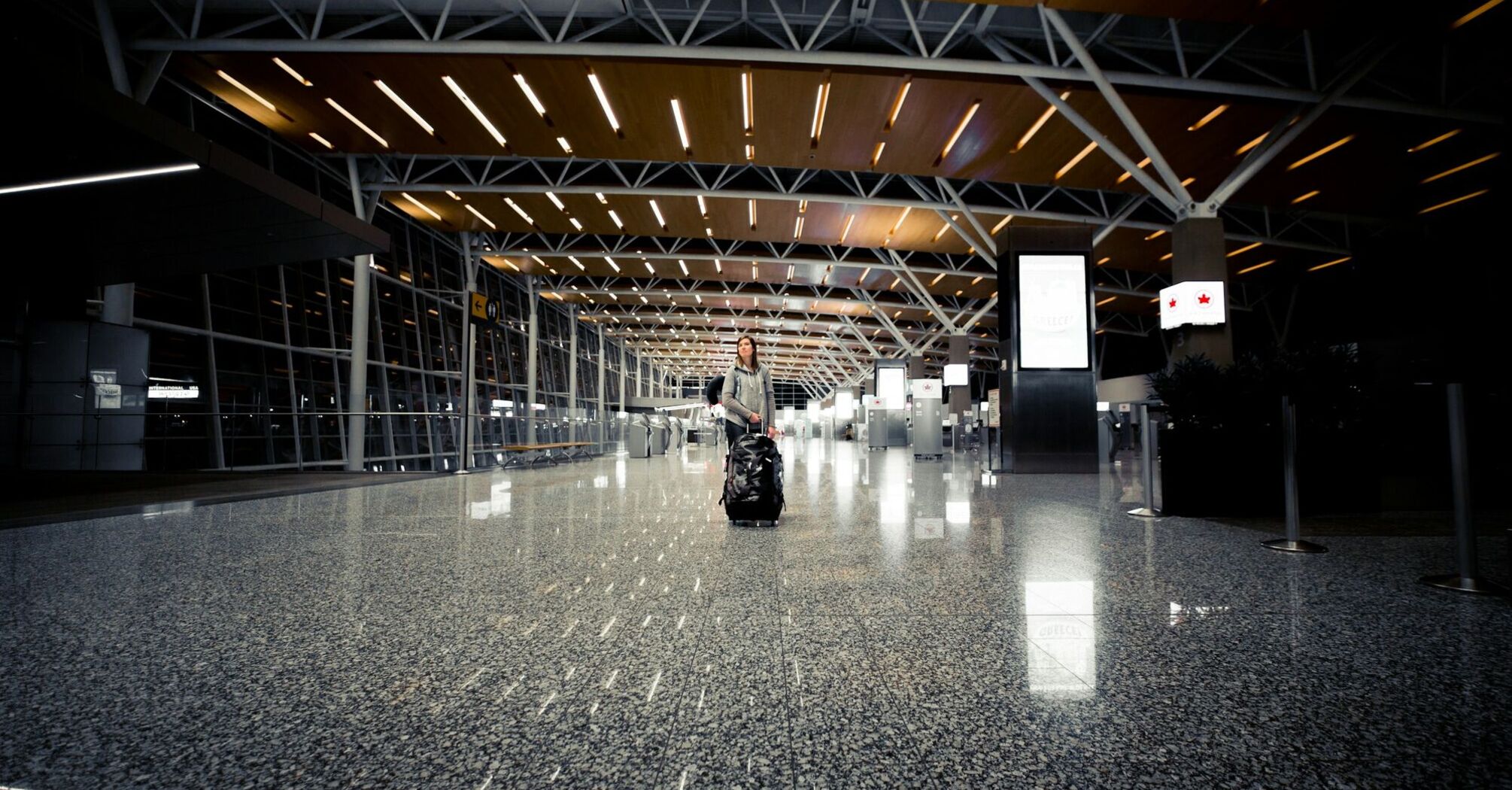 A solitary traveler with a rolling suitcase walks through the spacious, well-lit terminal of Calgary International Airport