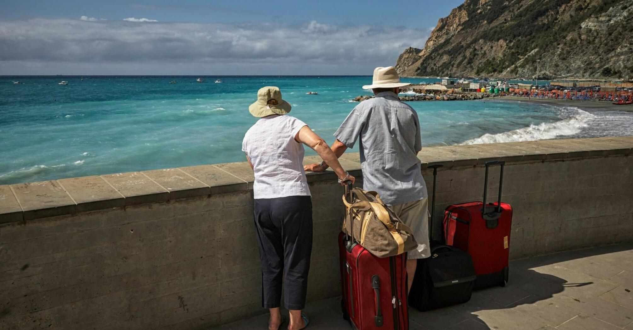 Two elderly travelers with suitcases looking at the beach