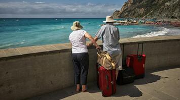Two elderly travelers with suitcases looking at the beach