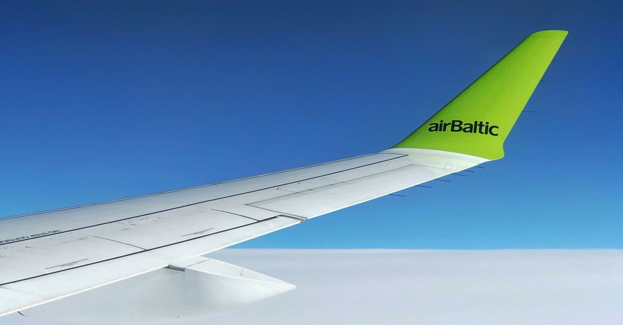 View from an airBaltic airplane window showing the wing and bright sky