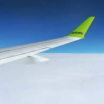 View from an airBaltic airplane window showing the wing and bright sky