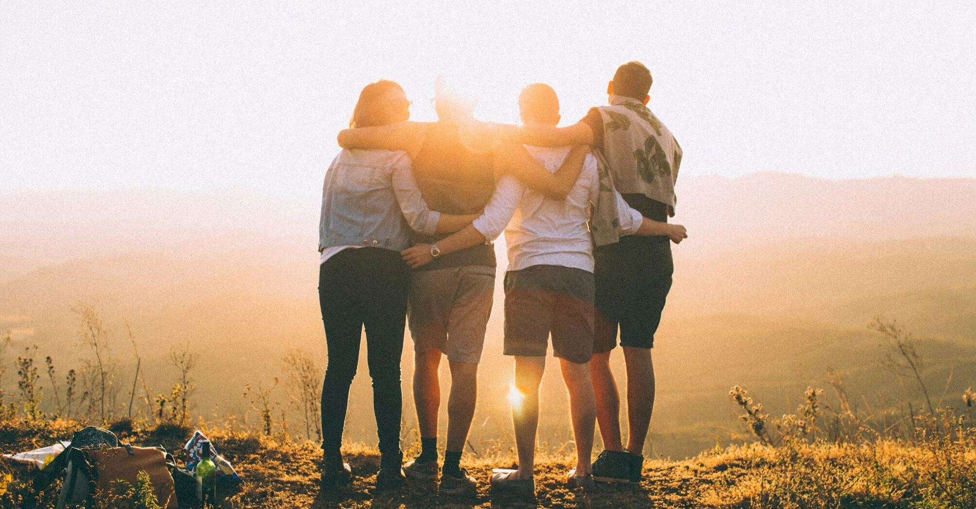 Four friends standing together, embracing at sunset