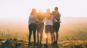 Four friends standing together, embracing at sunset