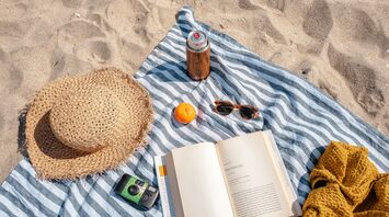 Beach setup with a hat, book, camera, sunglasses, and drink