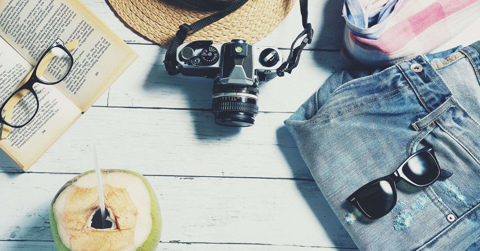Travel essentials including a camera, book, sunglasses, and hat