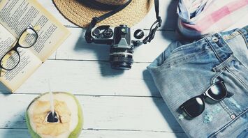 Travel essentials including a camera, book, sunglasses, and hat